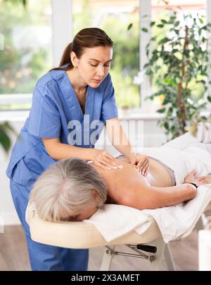 Femme âgée méconnaissable se couche face cachée sur le canapé et profiter de soins spa, massage des épaules Banque D'Images