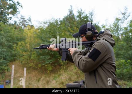 Un homme dans une veste verte tient un fusil et porte des écouteurs. Il est dans une forêt et il pratique le tir Banque D'Images