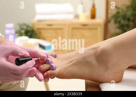 Pédicuriste professionnel peignant les ongles des orteils du client avec du vernis dans le salon de beauté, gros plan Banque D'Images