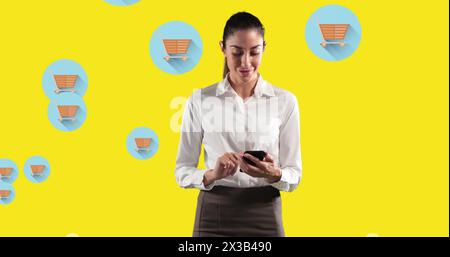 Image d'une femme utilisant un smartphone contre plusieurs icônes de panier d'achat sur fond jaune Banque D'Images