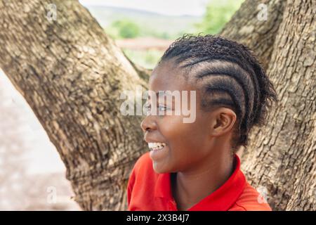 village african adolescent girl vue de profil, portant des tresses coiffure, debout devant un arbre dans la cour Banque D'Images
