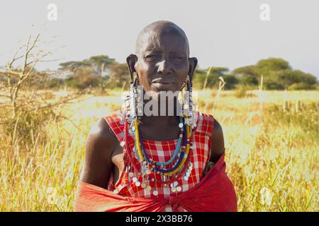 5 février 2024. Parc national d'Amboseli. Kenya : une femme adulte Massaï dans une robe rouge traditionnelle et des bijoux perlés se tient sur le fond de Banque D'Images