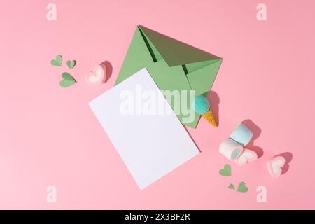 Guimauves, bonbons et coeurs en papier décorés sur fond rose avec un papier blanc et une enveloppe verte. Carte élégante pour la Journée internationale de la femme. Banque D'Images