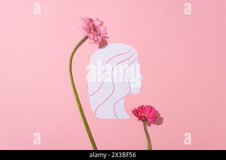 Concept de la Journée internationale de la femme avec un papier blanc coupé dans une forme de femme décorée de fleurs fraîches en couleur rose sur la surface. Vue de dessus. Un jour Banque D'Images