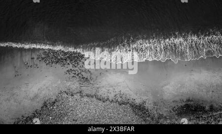 Vue aérienne d'un rivage serein avec des vagues, de la mousse et des galets en noir et blanc, vue aérienne de la plage Banque D'Images