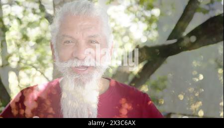 Image de taches de lumière et d'arbres sur un homme biracial senior souriant dans le jardin Banque D'Images