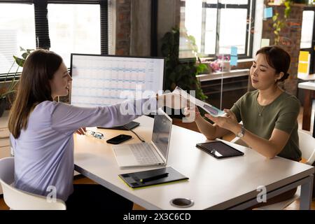 Professionnel asiatique mature examinant des documents avec une jeune collègue féminine caucasienne dans un mode Banque D'Images