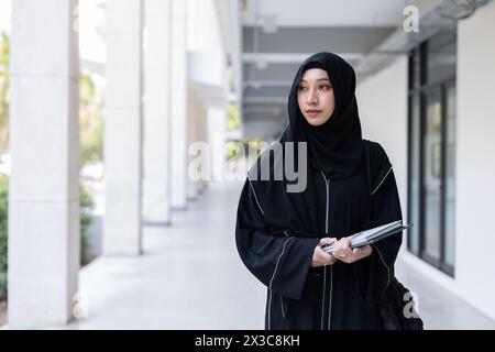 Université saoudienne niqab musulmane haute éducation dans le bâtiment du campus universitaire avec des livres de connaissances modernes. Arabe saoudienne noire tchador adolescente. Banque D'Images