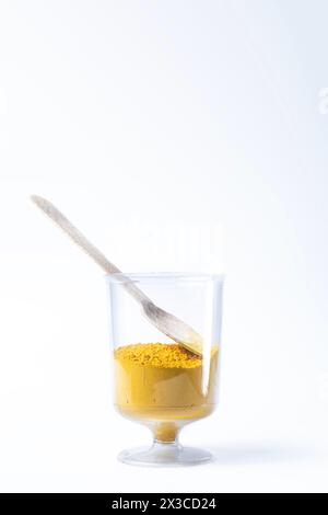 Sable en poudre holi jaune coloré dans une tasse en verre avec cuillère en bois sur fond blanc. Gros plan Banque D'Images