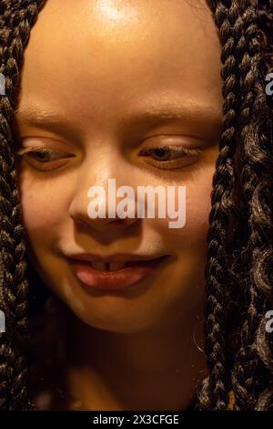 Cette image est un portrait tendre d'un enfant avec les yeux fermés et une expression sereine. Les tresses créent un motif texturé à travers le cadre, et la peau lisse de l'enfant est éclairée par une lueur douce et chaude. Ce moment capture un sentiment de paix et de simplicité enfant serein avec les yeux fermés et les tresses torsadées. Photo de haute qualité Banque D'Images