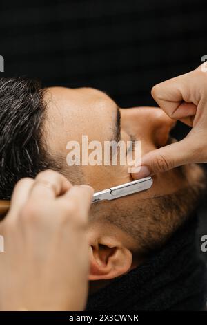 Un homme assis dans un salon de coiffure se faisant raser la barbe par le barbier Banque D'Images