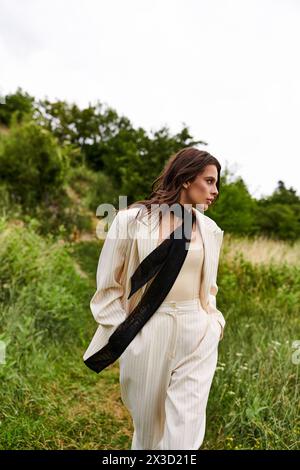 Une belle jeune femme en costume blanc et foulard noir profite de la brise estivale dans un champ serein. Banque D'Images