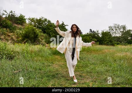 Une belle jeune femme en manteau blanc marche gracieusement à travers un champ paisible, profitant de la brise estivale. Banque D'Images
