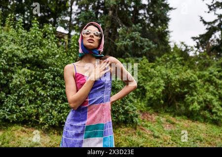 Une jeune femme vibrante portant une serviette colorée se tient gracieusement dans un champ ensoleillé, incarnant la joie et la beauté dans la nature. Banque D'Images