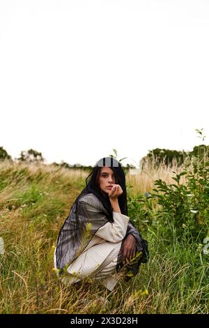 Une belle jeune femme en tenue blanche agenouillée dans un champ de hautes herbes, profitant de la brise d'été. Banque D'Images