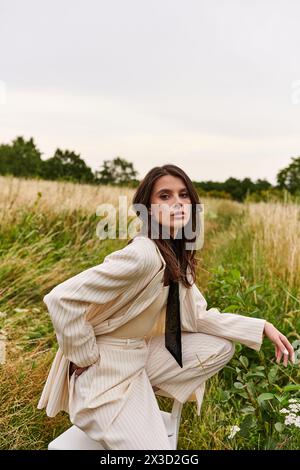 Une belle jeune femme dans un costume blanc et cravate se tient gracieusement dans un champ, profitant de la brise de l'été. Banque D'Images