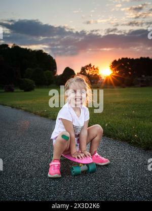 Belle fille heureuse chevauchant skateboard avec bandaid sur le genou Banque D'Images