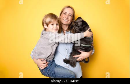 Heureuse mère avec son fils et chien schnauzer debout isolé sur fond jaune. Banque D'Images