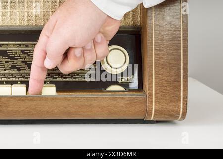 Une vraie radio des années 60 La main d'un homme tourne sur le bouton. Plan de gros plan. Sur fond blanc. Traces du temps. Banque D'Images