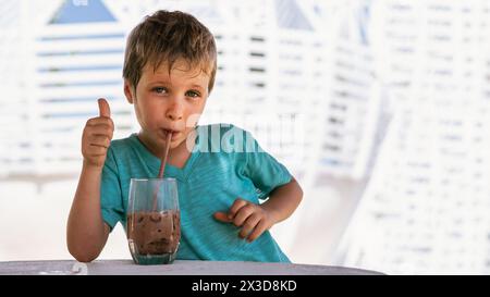 Heureuse enfance. Garçon buvant du thé au chocolat avec de la glace dans le temps chaud de la journée d'été. Mignon amoureux des bonbons et des choses savoureuses. Affiche pouces vers le haut. Banque D'Images