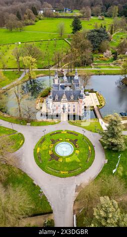 Huizingen, Belgique, 26 mars 2024, cette photographie aérienne met en valeur l'opulent château du domaine de Huizingen, niché au cœur de la Belgique. La structure ornée est entourée de jardins méticuleusement entretenus et d'un étang réfléchissant, avec le cadran solaire en évidence à l'avant-garde. La verdure luxuriante et l'art paysager accentuent la grandeur du domaine et son harmonie avec la nature. Vue aérienne majestueuse du Château dans le domaine de Huizingen, Belgique. Photo de haute qualité Banque D'Images