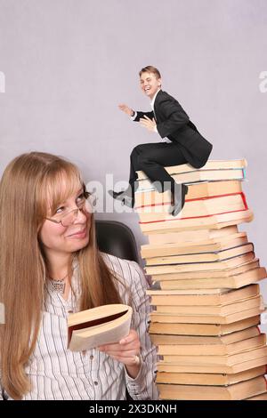 Collage avec la jeune jolie fille lit le livre à haute voix au petit homme d'affaires assis sur pile de livres, tout le monde est souriant Banque D'Images