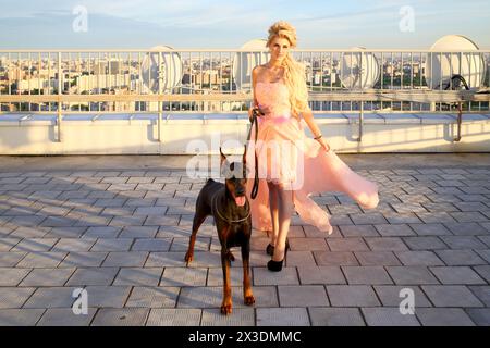 Portrait de belle blonde dans une robe rose avec le Doberman sur le toit Banque D'Images