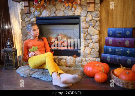 La jeune fille avec des feuilles est assise dans la pièce avec des citrouilles devant une cheminée Banque D'Images