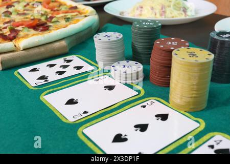 Jouer aux cartes et aux jetons sur une table de jeu verte près d'une pizza sur une assiette et des pâtes Banque D'Images