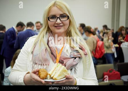 Jeune femme blonde se tient debout tenant la plaque avec sandwich et croissant dans l'auditorium, dof peu profond. Banque D'Images