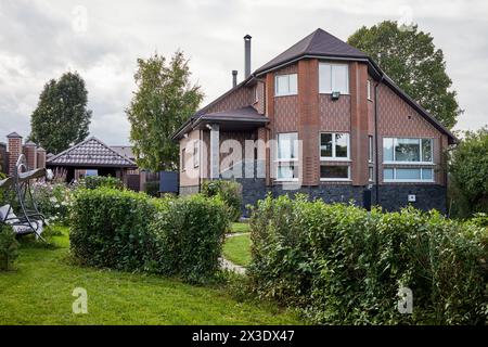 Maison de cottage moderne en brique rouge et jardin avec fleurs, buissons, arbres. Banque D'Images