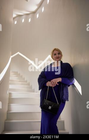 Femme blonde en robe bleue se tient sur les escaliers penchés au mur. Banque D'Images