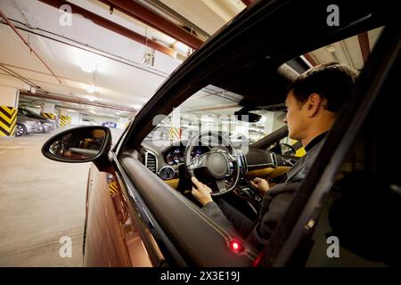 L'homme est assis sur le siège du conducteur dans la voiture moderne au parking souterrain. Banque D'Images