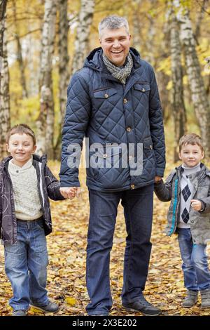 Homme souriant et deux petits garçons se tiennent la main dans le parc d'automne. Banque D'Images