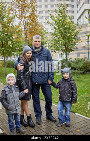 Père, fille et deux petits fils se tiennent sur un sentier pavé le jour pluvieux d'automne. Banque D'Images