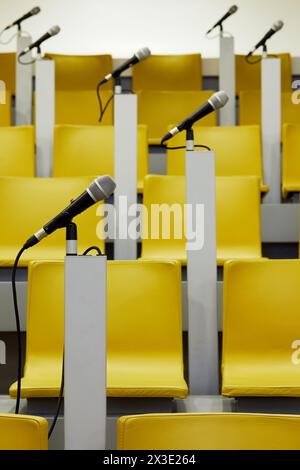 Microphones dans des supports sur des supports dans un auditorium avec des chaises jaunes. Banque D'Images