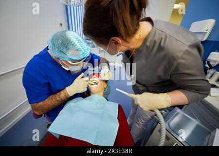 MOSCOU, RUSSIE - DEC 25, 2017 : stomatologue applique un gel spécial sur la dent de la femme (MR) dans le fauteuil dentaire, assistant se tient près. Banque D'Images