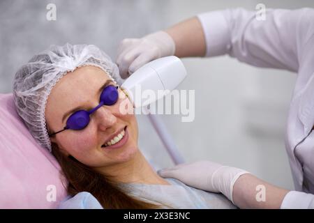 Femme se trouve sur la chaise cosmétologique pendant la procédure sur son visage dans le bureau de cosmétologie. Banque D'Images