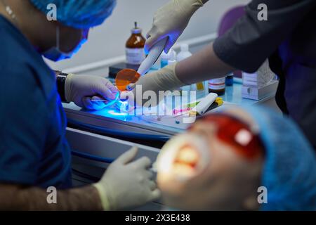 Dentiste et assistant préparent l'implant dentaire sur la table médicale en utilisant la lampe ultraviolette. Banque D'Images