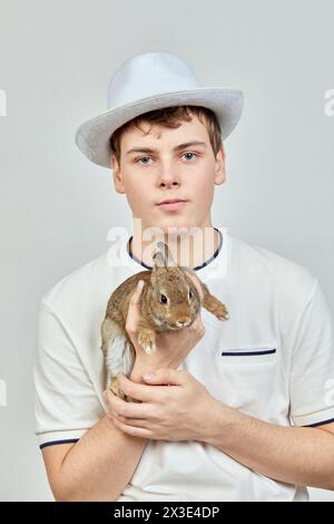 Portrait en demi-longueur d'un garçon dans un chapeau tenant un lapin dans les bras. Banque D'Images