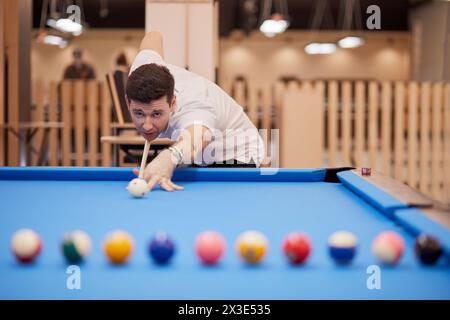 Homme en chemise blanche à col polo vise des balles sur la table de billard dans le club de billard. Banque D'Images