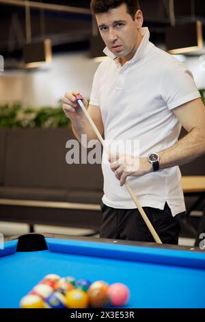 Homme dans la chemise blanche à col polo craies pointe de bâton de queue debout près de la table de billard dans le club. Banque D'Images