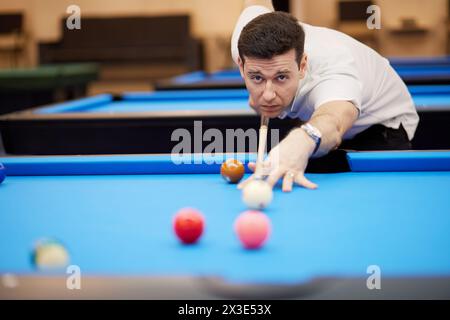 L'homme vise la balle blanche avec le bâton de queue sur la table de billard dans le club. Banque D'Images