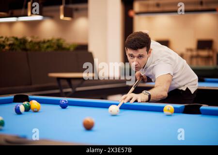 Homme en chemise blanche à col polo vise des balles sur la table de billard dans le club. Banque D'Images