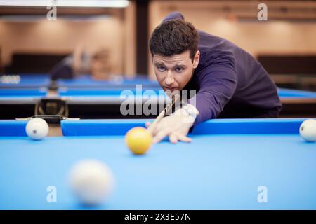 L'homme en chemise bleu foncé vise la boule jaune de queue jouant au billard. Banque D'Images