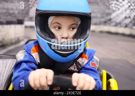 Petit garçon drôle dans le casque conduit dans le Go-kart sur la piste pendant la compétition Banque D'Images