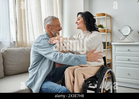 Une femme en fauteuil roulant embrasse son mari, montrant amour et soutien dans leur salon. Banque D'Images