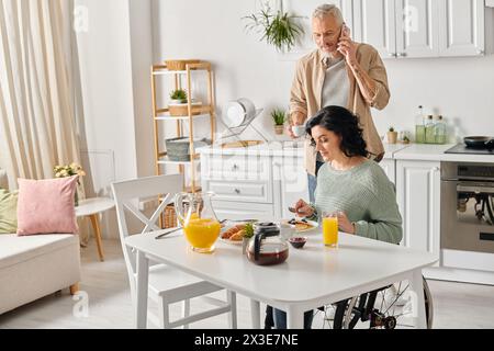 Un mari et une femme handicapée dans un fauteuil roulant, se tiennent côte à côte à une table de cuisine, créant une scène réconfortante. Banque D'Images