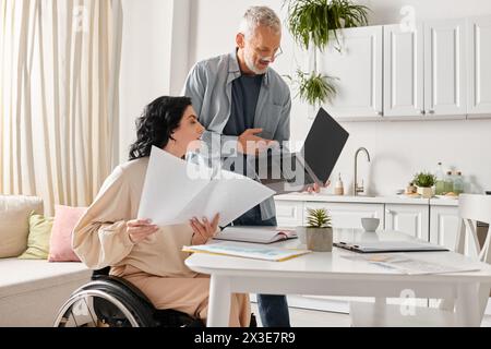 Une femme en fauteuil roulant s'assoit attentivement à l'aide d'un ordinateur portable, engrossé dans son écran, dans un cadre de cuisine domestique. Banque D'Images