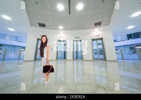 Femme en costume avec sac dans le hall avec portes d'ascenseur transparentes, collage Banque D'Images